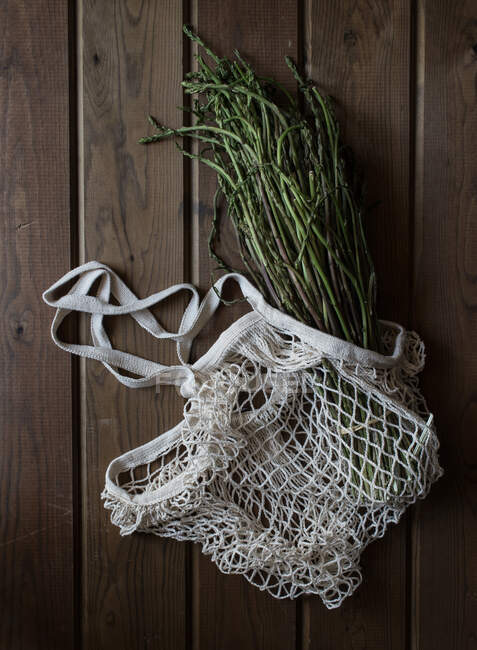 From above of white string bag with big bundle of fresh green asparagus on wooden table — Stock Photo