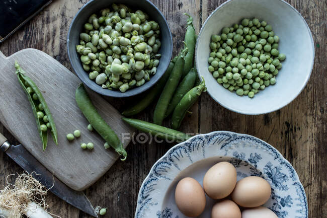 Von oben am Seil frische grüne Erbsen in Schüssel und Eier auf Holztisch beim Kochen — Stockfoto