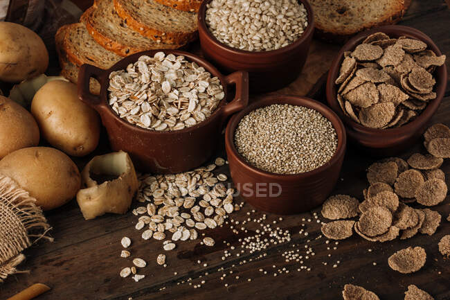 From above cereals oatmeal seeds in bowls potatoes and sliced bread on wooden background — Stock Photo