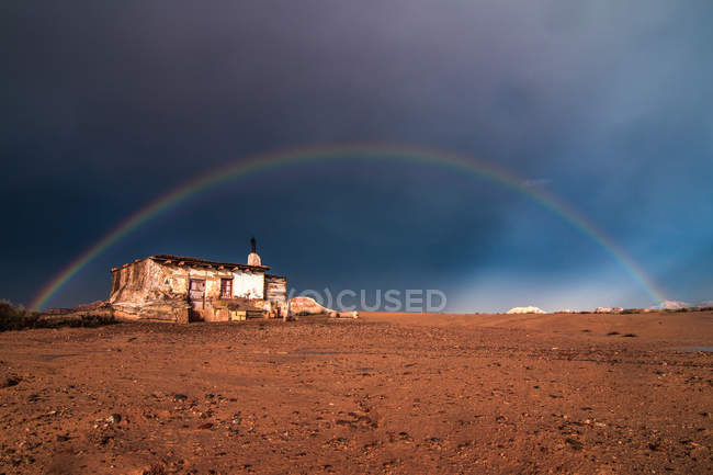 Vieille maison solitaire dans le désert et arc-en-ciel dans le ciel orageux — Photo de stock