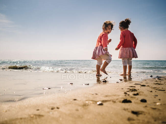 Cheerful cute twins playing on sandy seashore on background of clear sky — Stock Photo