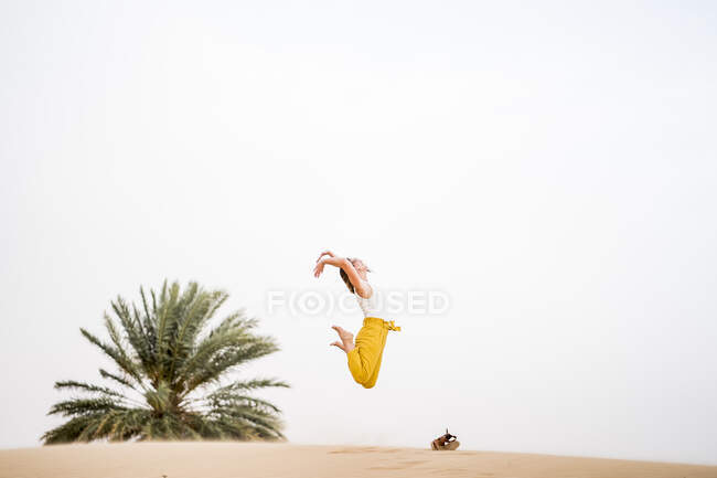 Cheerful stylish blonde woman jumping in the middle of the desert of Morocco — Stock Photo