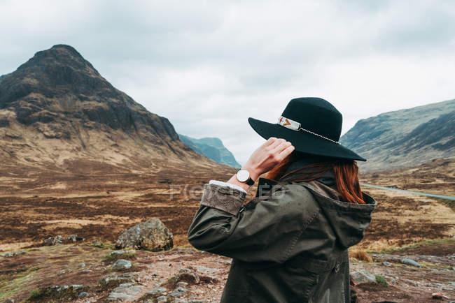 Donna che indossa e tiene il cappello in piedi contro le pittoresche montagne della Scozia — Foto stock