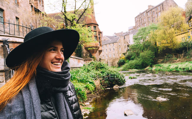 Femme rousse dans un beau paysage de vieux bâtiments de maçonnerie avec rivière peu profonde coulant parmi les buissons verts, Écosse — Photo de stock