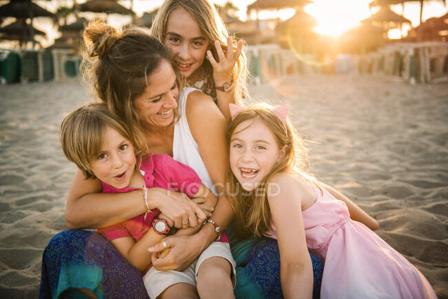 Mulher com filhas brincalhões e filho deitado na praia de areia se divertindo juntos — Fotografia de Stock