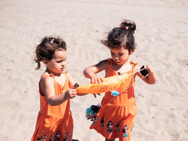 Little sisters in bright orange dresses playing together on seaside in sunny day — Stock Photo