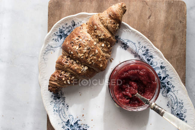Knusprige Croissants und Erdbeermarmelade auf Teller auf Holzbrett serviert — Stockfoto