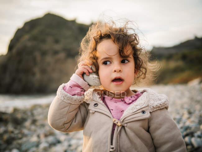 Портрет милої дівчинки, яка слухає ковзанку з величезною увагою, відпочиваючи на кам'яному узбережжі — стокове фото