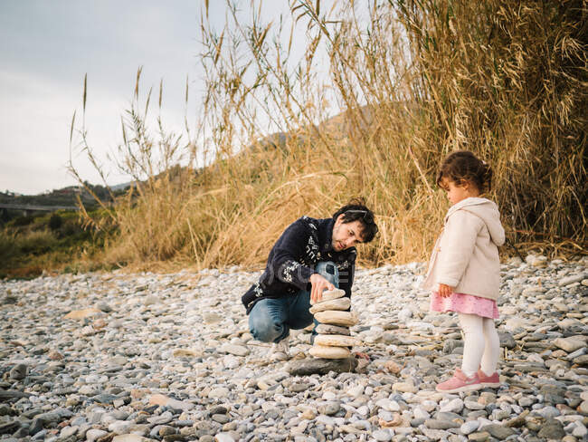 Jeune homme et mignon tout-petit fille jouer ensemble sur le bord de mer pierreux — Photo de stock