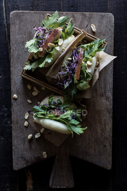 Сверху на деревянной доске подаются бутерброды Гуа Бао с беконом и петрушкой. — стоковое фото