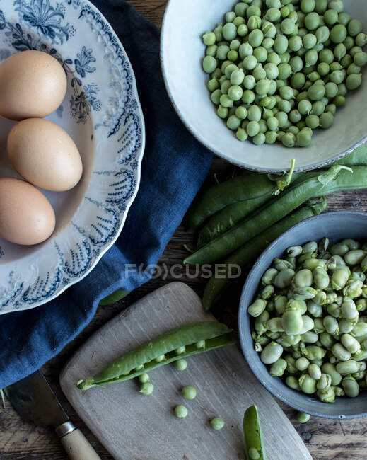 Dall'alto di corda piselli verdi freschi in boccia e uova su tavolo di legno durante cottura — Stock Photo