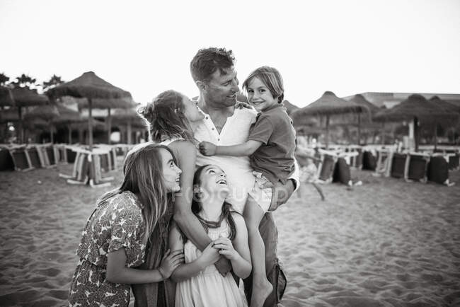 Adult loving man and woman with daughters looking at boy son standing together on beach in back lit , black and white photo — Stock Photo