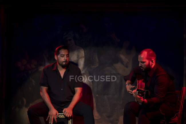 Uomini ispanici che suonano percussioni e chitarra acustica durante le esibizioni di flamenco sul palco buio — Foto stock