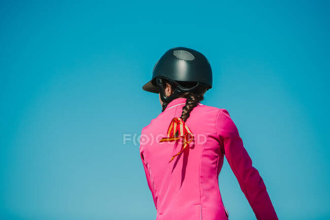 Visão traseira do anônimo menina jockey no cavalo montando na pista de corridas contra um céu azul em um dia ensolarado — Fotografia de Stock