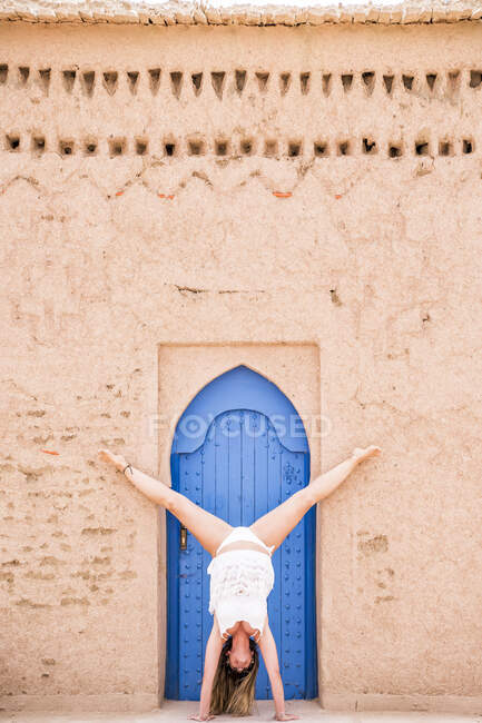 Frau in weißer Bademode zeigt Handstand vor orientalisch blauer Tür in Steinmauer, Marokko — Stockfoto