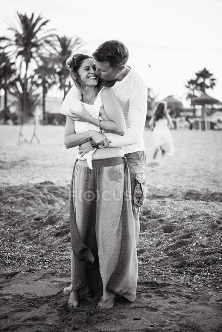 Черное и белое от взрослых любящих мужчин и женщин, обнимающих и целующихся на пляже — стоковое фото