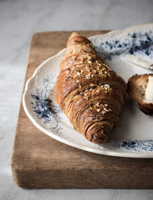 Closeup of golden crunchy croissant with grains served on plate on wooden board — Stock Photo