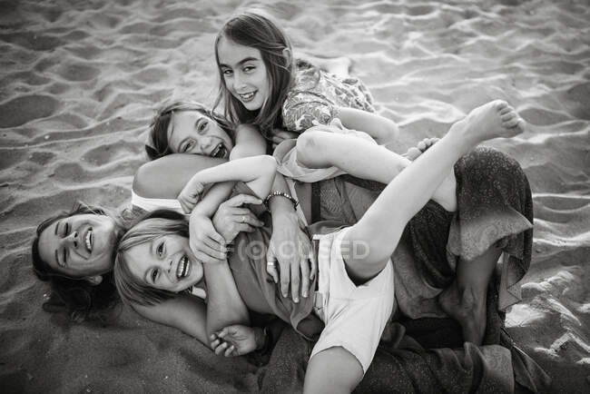 Preto e branco de mulher com filhas brincalhões e filho deitado na praia de areia se divertindo juntos — Fotografia de Stock