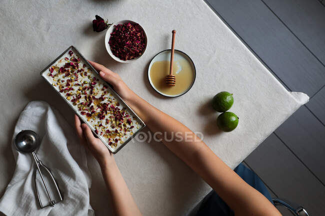 Hands of anonymous female putting container with delicious cheesecake on table near limes and honey with spices — Stock Photo
