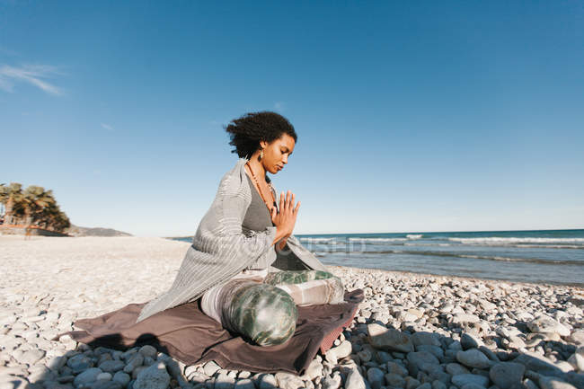 Afro-americano giovane donna meditando in loto yoga postura sulla spiaggia di sabbia in giorno luminoso — Foto stock