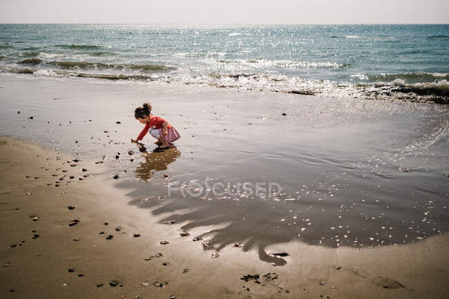 Side view of cute female toddler playing on sandy shore on background of calm sea — Stock Photo