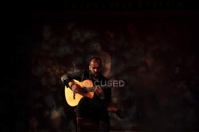 Calvo ragazzo barbuto suonare la chitarra acustica mentre seduto sul palco durante la performance di flamenco — Foto stock