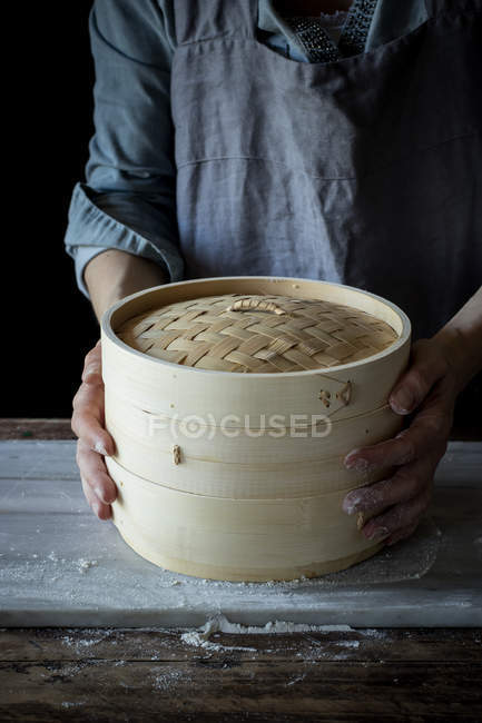 Midsection of person holding bamboo steamer on wooden table — Stock Photo