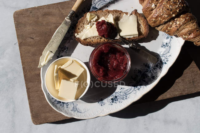 Crujiente croissant y tostadas con mantequilla y mermelada de fresa servido en tablero de madera - foto de stock
