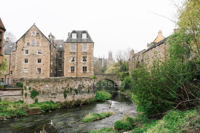 Landscape of old masonry buildings with shallow river flowing among green bushes, Scotland — Stock Photo