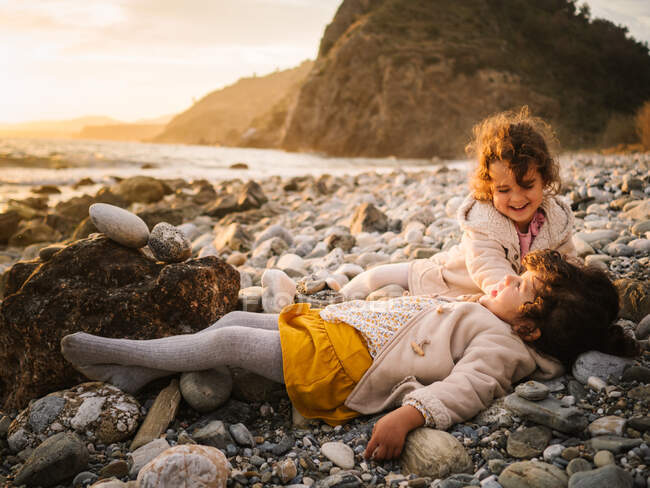 Toddler female twins playing on stony seashore on background of calm water — Stock Photo