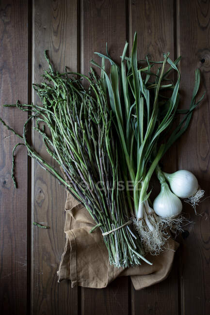 De cima do pacote de espargos verdes e bolbos de cebola fresca com hastes verdes na mesa de madeira — Fotografia de Stock