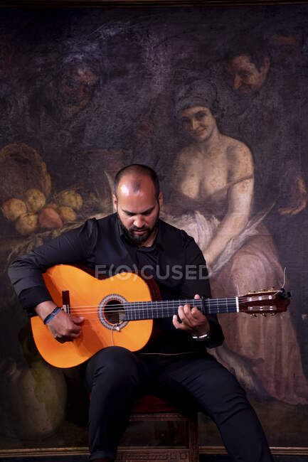 Calvo barbudo tocando la guitarra acústica sentado en el escenario durante la actuación flamenca — Stock Photo