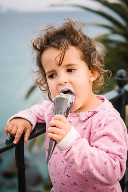 Portrait of charming pensive toddler girl eating ice-cream cornet outdoors — Stock Photo