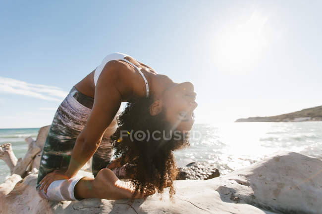 Gros plan de jeune femme attrayante afro-américaine debout dans le pont de posture de yoga sur fond d'eau calme dans la journée ensoleillée — Photo de stock