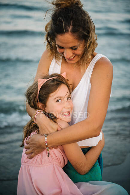 Lächelnde erwachsene Frau mit charmantem Mädchen, das sie umarmt und in die Kamera schaut — Stockfoto