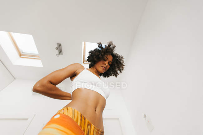 African American attractive young woman performing yoga posture with hands behind back in light room — Stock Photo