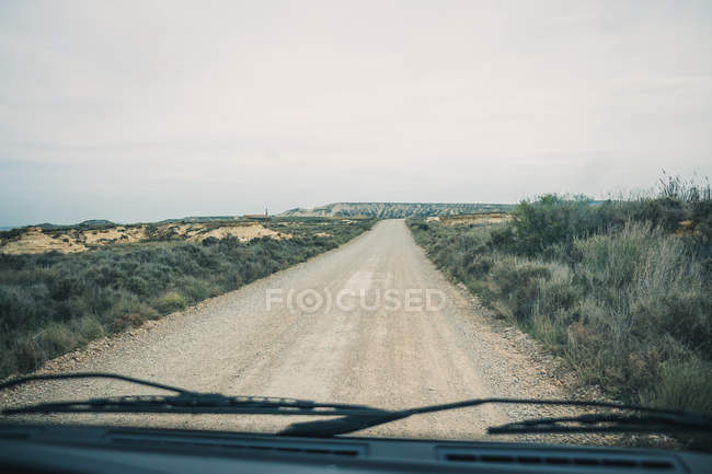 Estrada vazia jogar janela de carro levando entre campos com vegetação — Fotografia de Stock