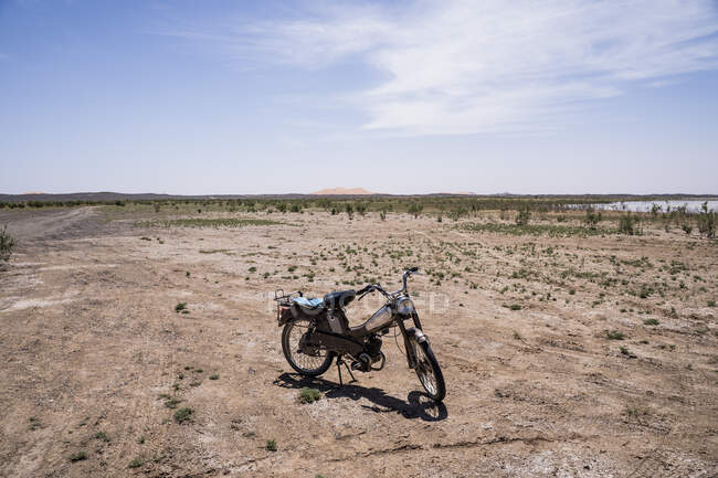 Vélo solitaire sur un terrain désertique sablonneux sous un ciel bleu clair au soleil, Maroc — Photo de stock