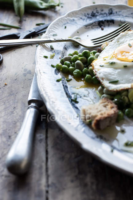 Крупним планом подається тарілка з обсмаженим зеленим горохом і смаженим яйцем на дерев'яному столі — стокове фото