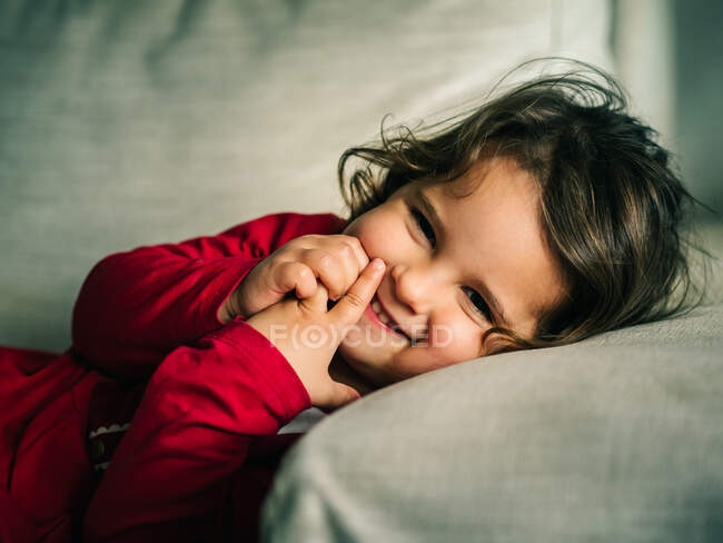 Adorabile ragazza in abito rosso sorridente mentre riposa sul cuscino a casa — Foto stock