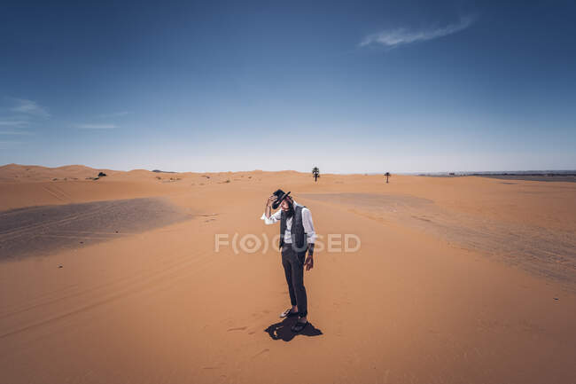 Бородатый мужчина в ковбойском костюме смотрит вниз, стоя в пустыне на фоне голубого неба — стоковое фото
