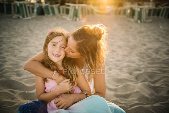 Erwachsene Frau küsst schönes Mädchen, das sich am Sandstrand im Sonnenuntergang liebevoll umarmt — Stockfoto