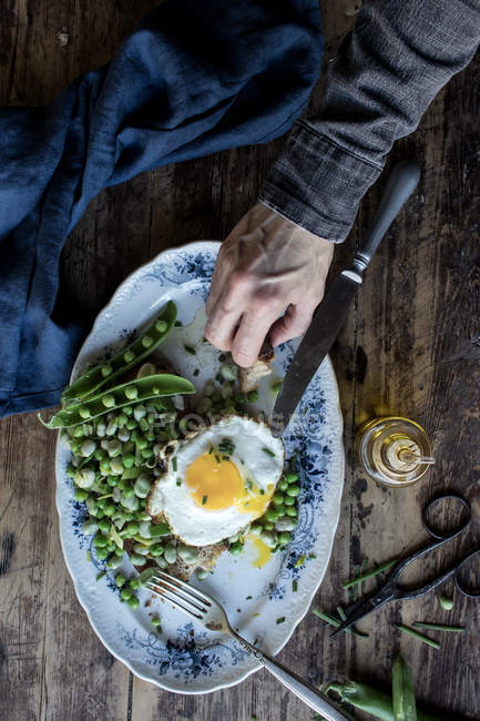 Дегустація людської руки з поданої тарілки з зеленим горохом та смаженим яйцем на дерев'яному столі — стокове фото