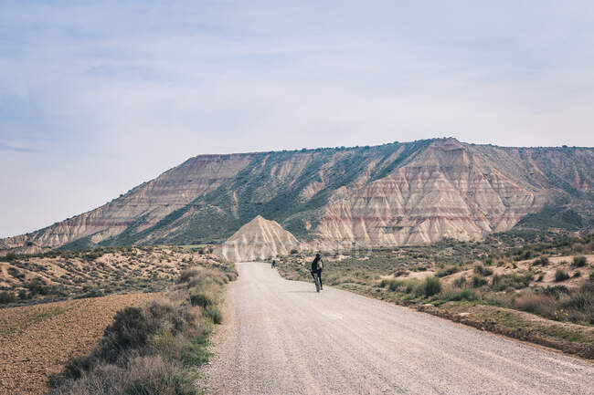 Человек ездит на велосипедах по дороге в пустынные холмы — стоковое фото