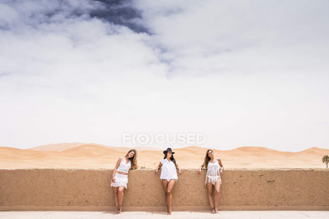 Eine Reihe von Frauen in weißer Strandkleidung posiert am Steinzaun auf der Terrasse vor endloser Wüste, Marokko — Stockfoto