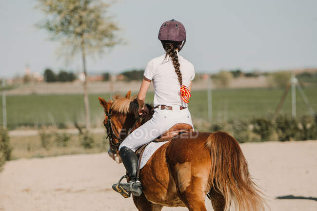 Vista posteriore di anonima ragazza fantino a cavallo in pista in una giornata di sole — Foto stock