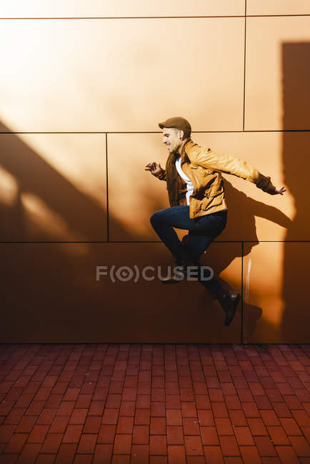 Позитивний молодий чоловік в стильному вбранні стрибає біля стіни сучасної будівлі в сонячний день — стокове фото
