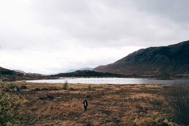 Erwachsener Mann mit Rucksack steht in malerischem abgelegenen Tal, Berge und See schauen weg — Stockfoto