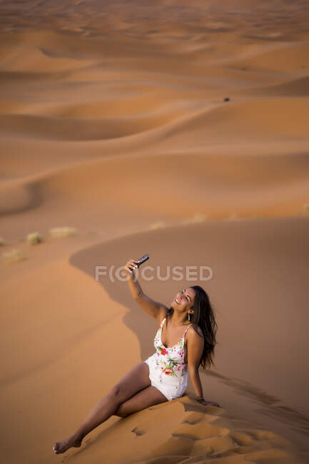 Jeune femme prenant selfie avec téléphone au milieu du désert de sable, Maroc — Photo de stock