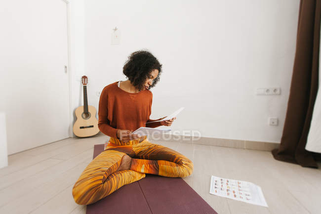 Afro-Américaine jolie jeune femme assise avec les jambes croisées et vérifier les papiers de routine — Photo de stock